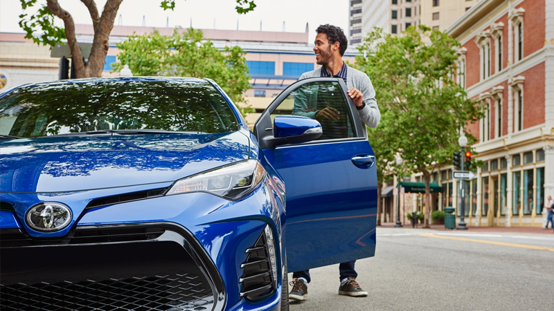 A smiling man next to his pre owned Toyota Corolla